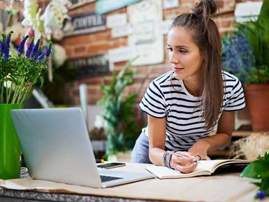 Woman looking at a laptop whilst writing on a piece of paper