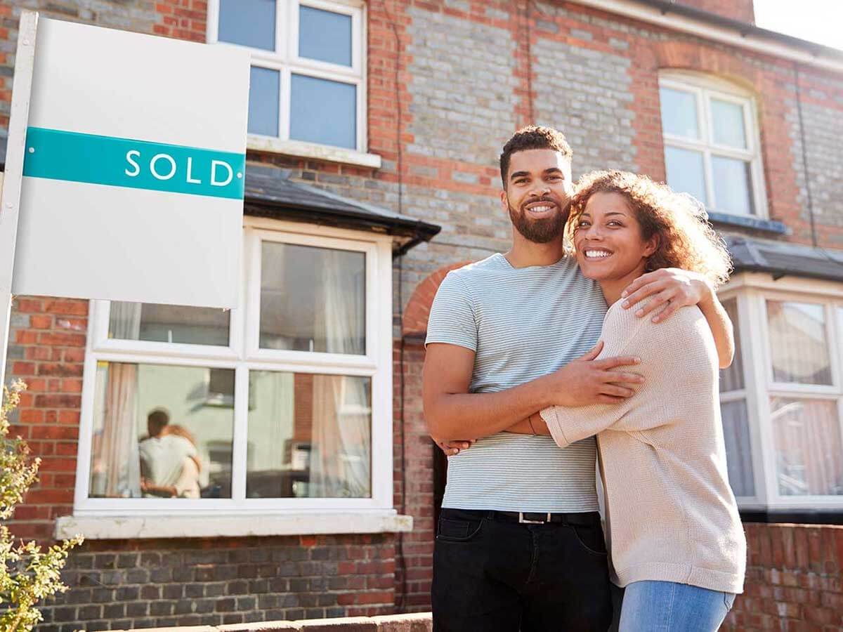 A young couple standing outside a house with a sold sign 