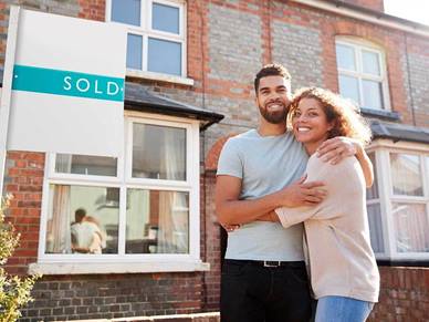 A young couple standing outside a house with a sold sign 