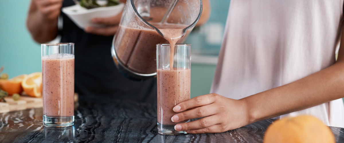 Woman in kitchen pooring smoothie eating cereal